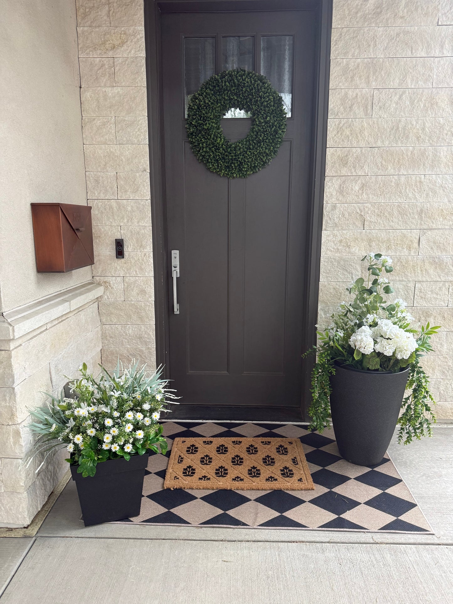 Front door with a wreath, potted plants, and a doormat on a checkered floor.